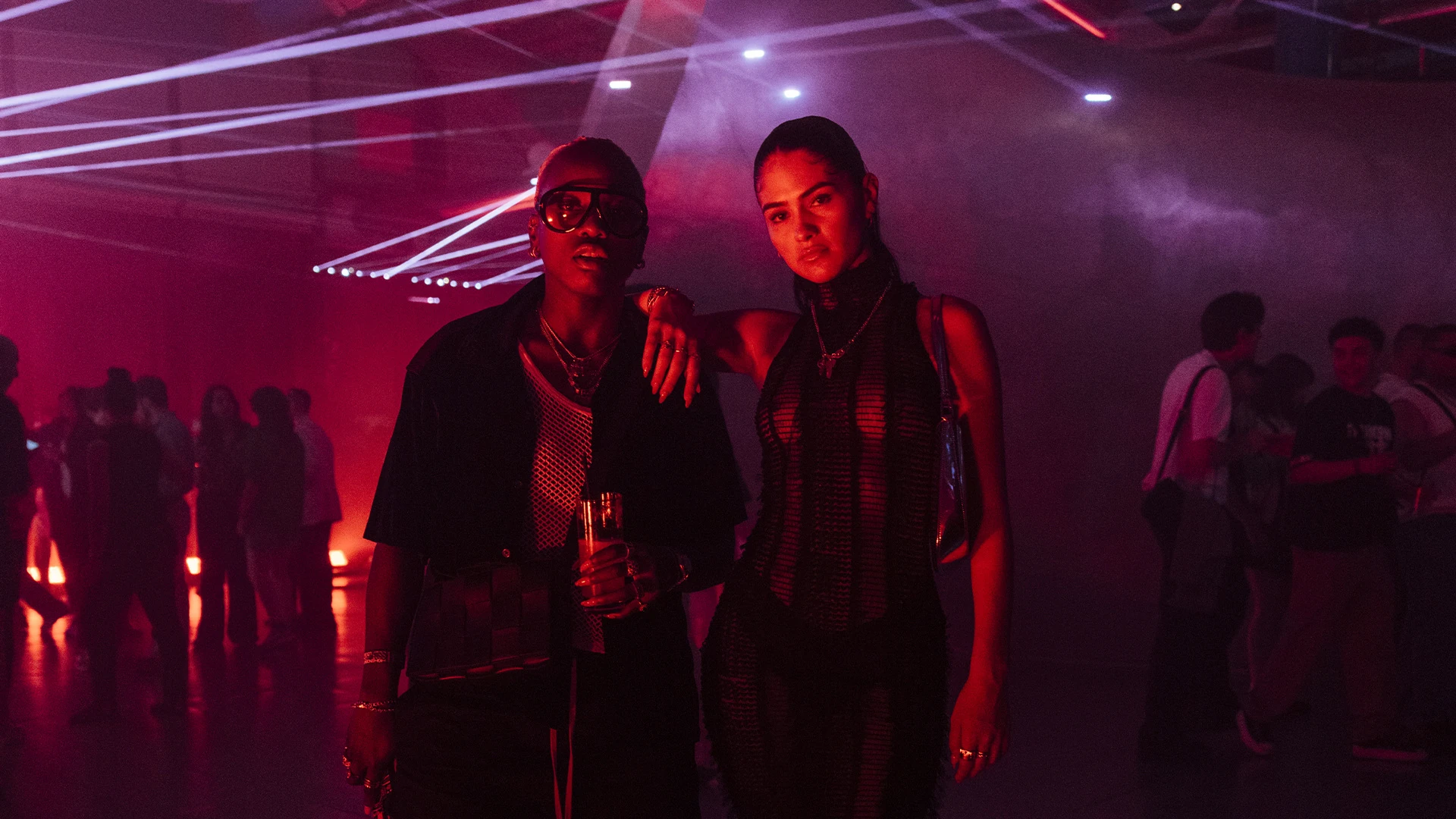Two guests posing in a magenta-lit room, laser lines crossing the wall behind them.