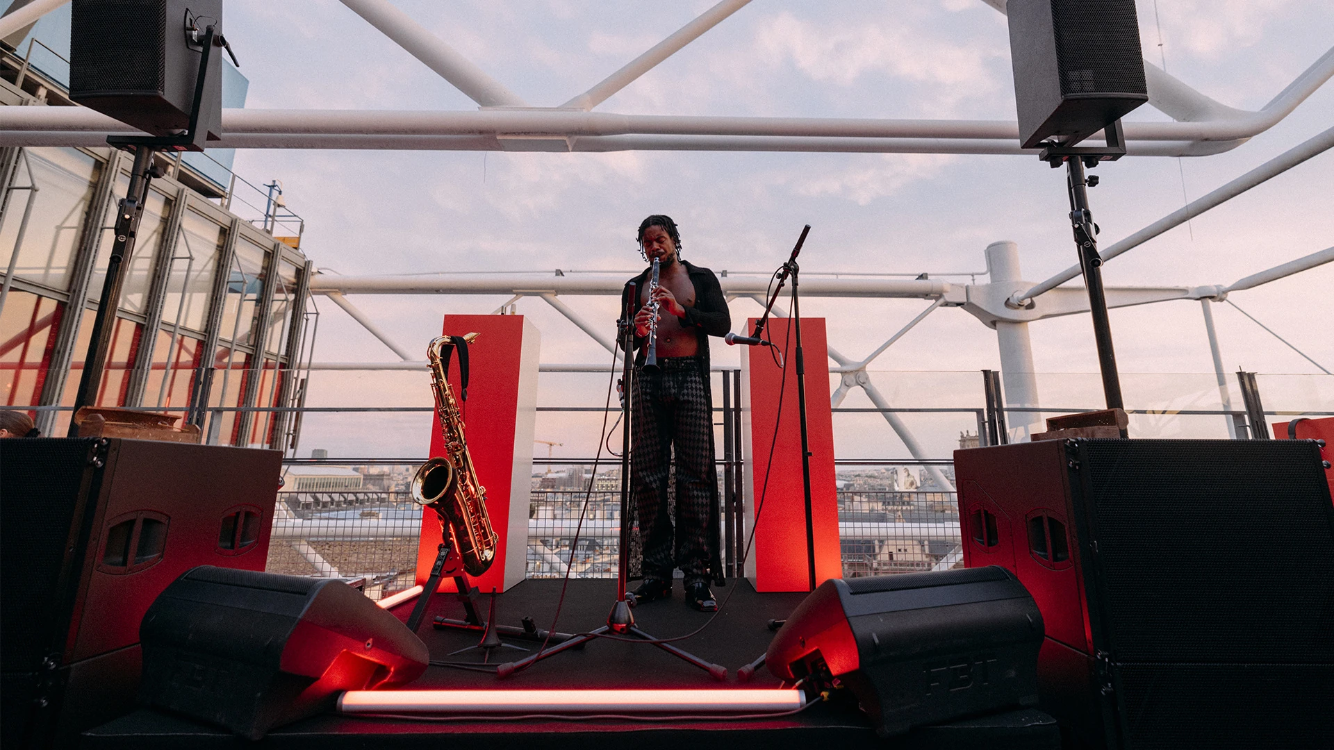 CKTRL performing with a saxophone on a rooftop stage lit in red.