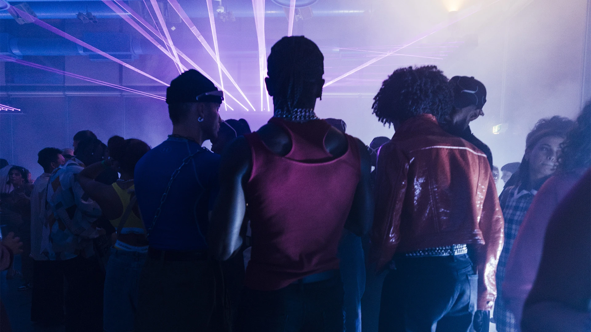 Guests seen from behind facing the stage as violet lasers fan out overhead.