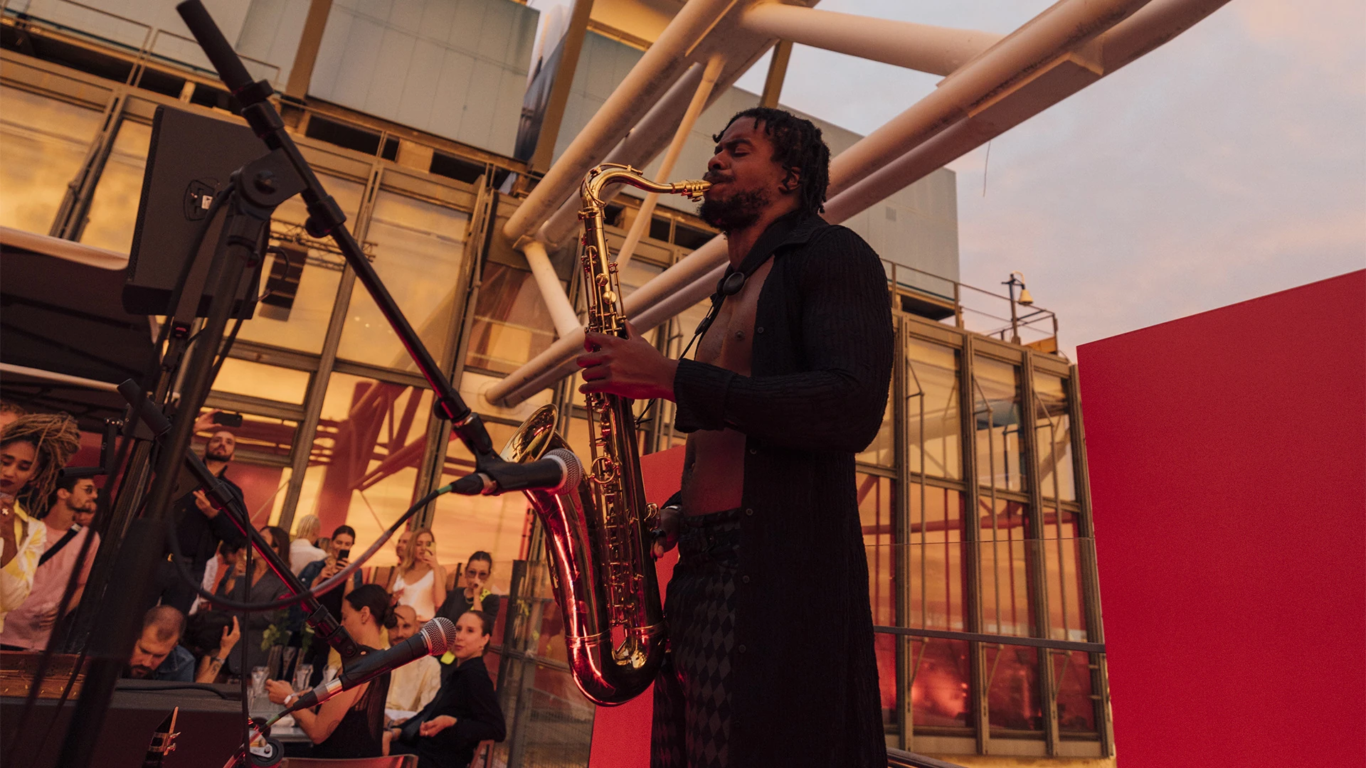 CKTRL playing saxophone on a rooftop stage at dusk.
