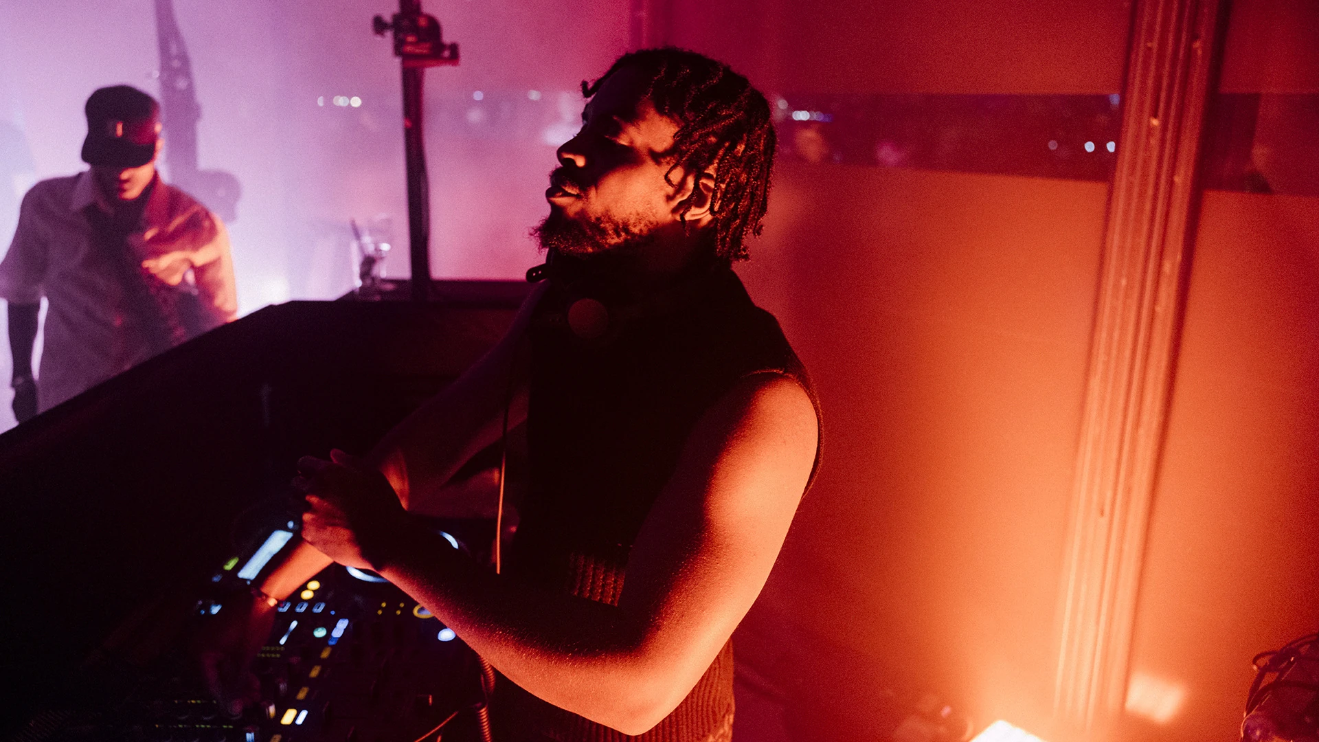A performer at the decks in front of a wall of orange haze and light.