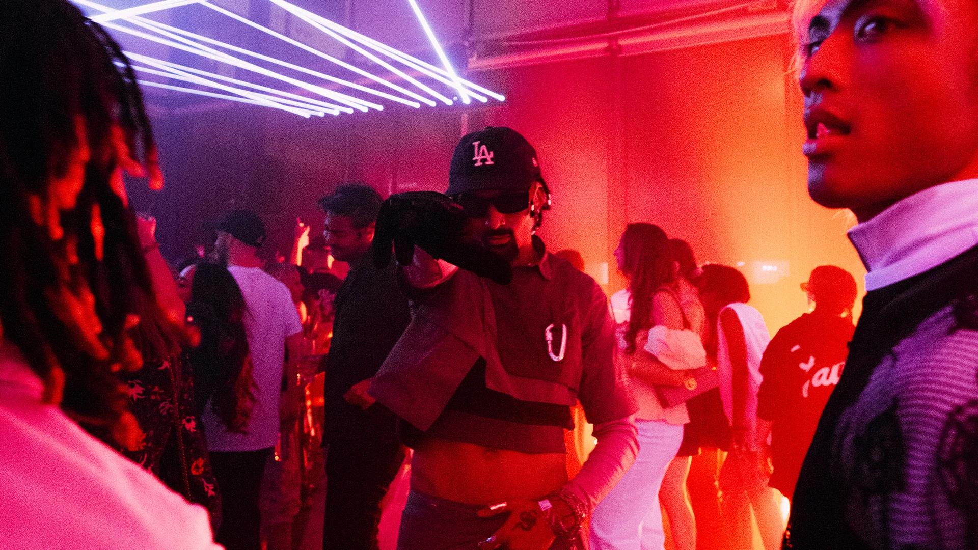 A crowded dance floor under white laser beams and red haze.