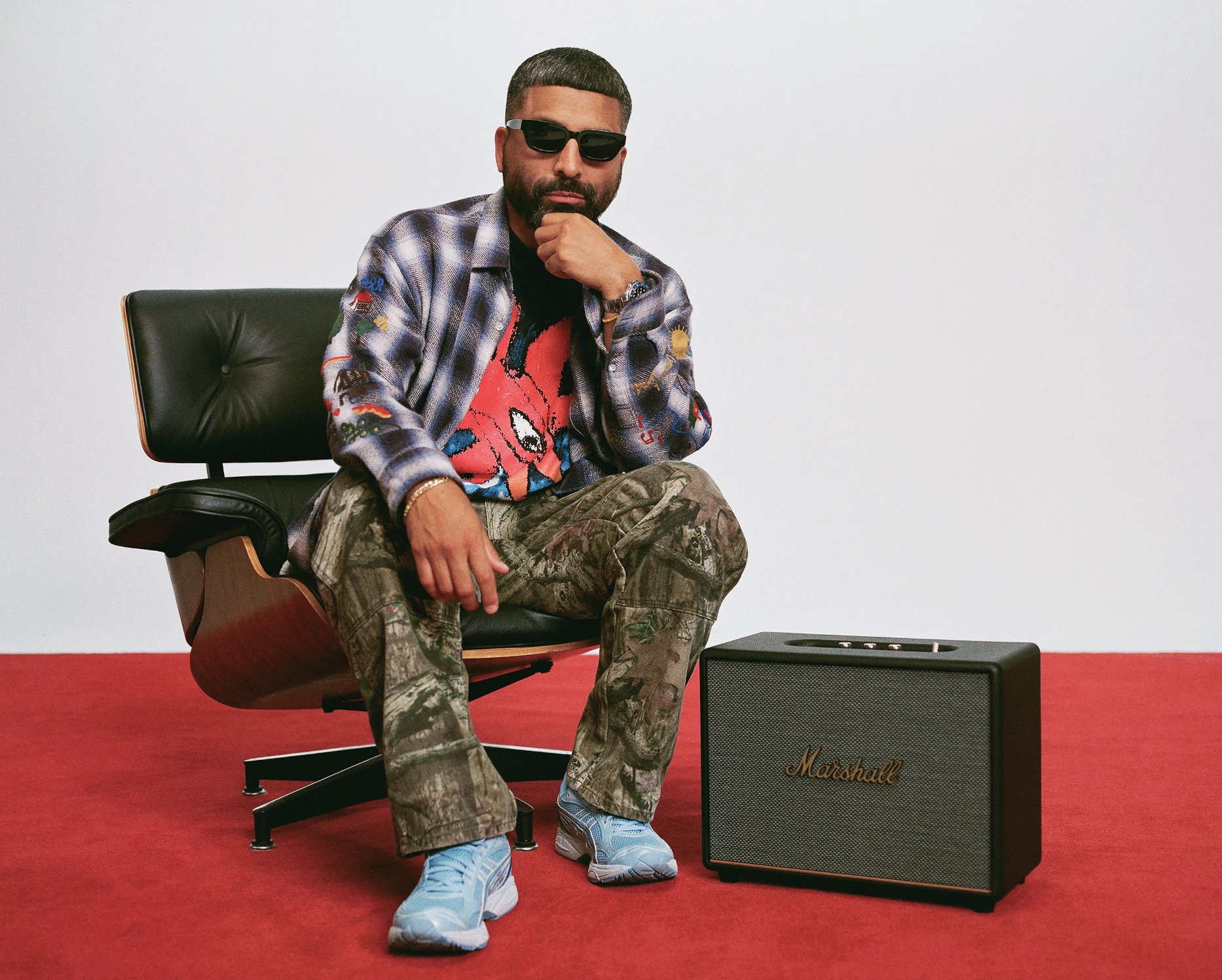Angelo Baque seated in a leather lounge chair beside a Marshall speaker on a red floor.