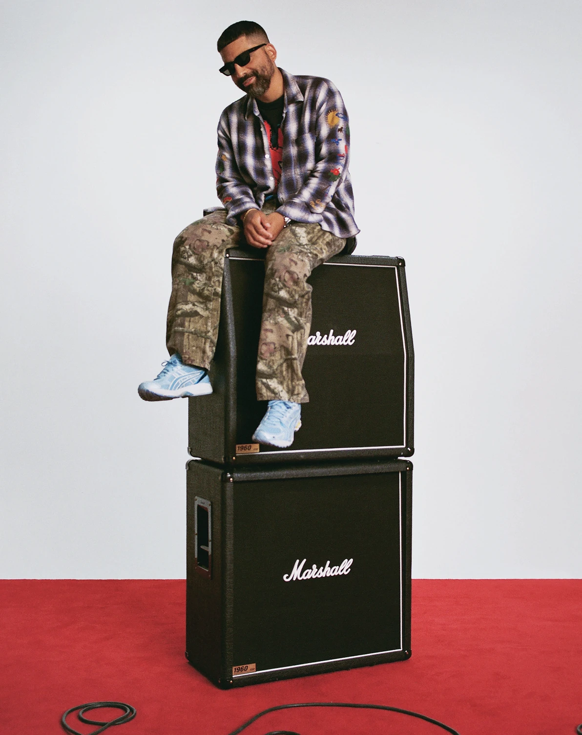 Angelo Baque sitting on top of a stack of two Marshall speaker cabinets.