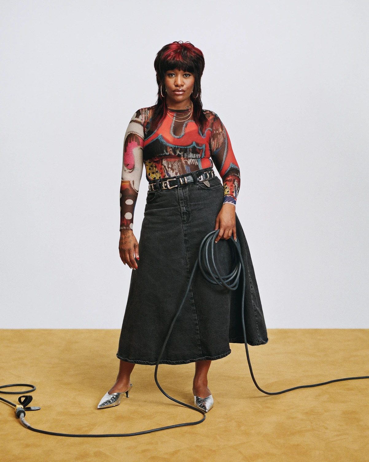 Shanel Campbell standing with a coiled cable in a black denim skirt, cables trailing across the floor.