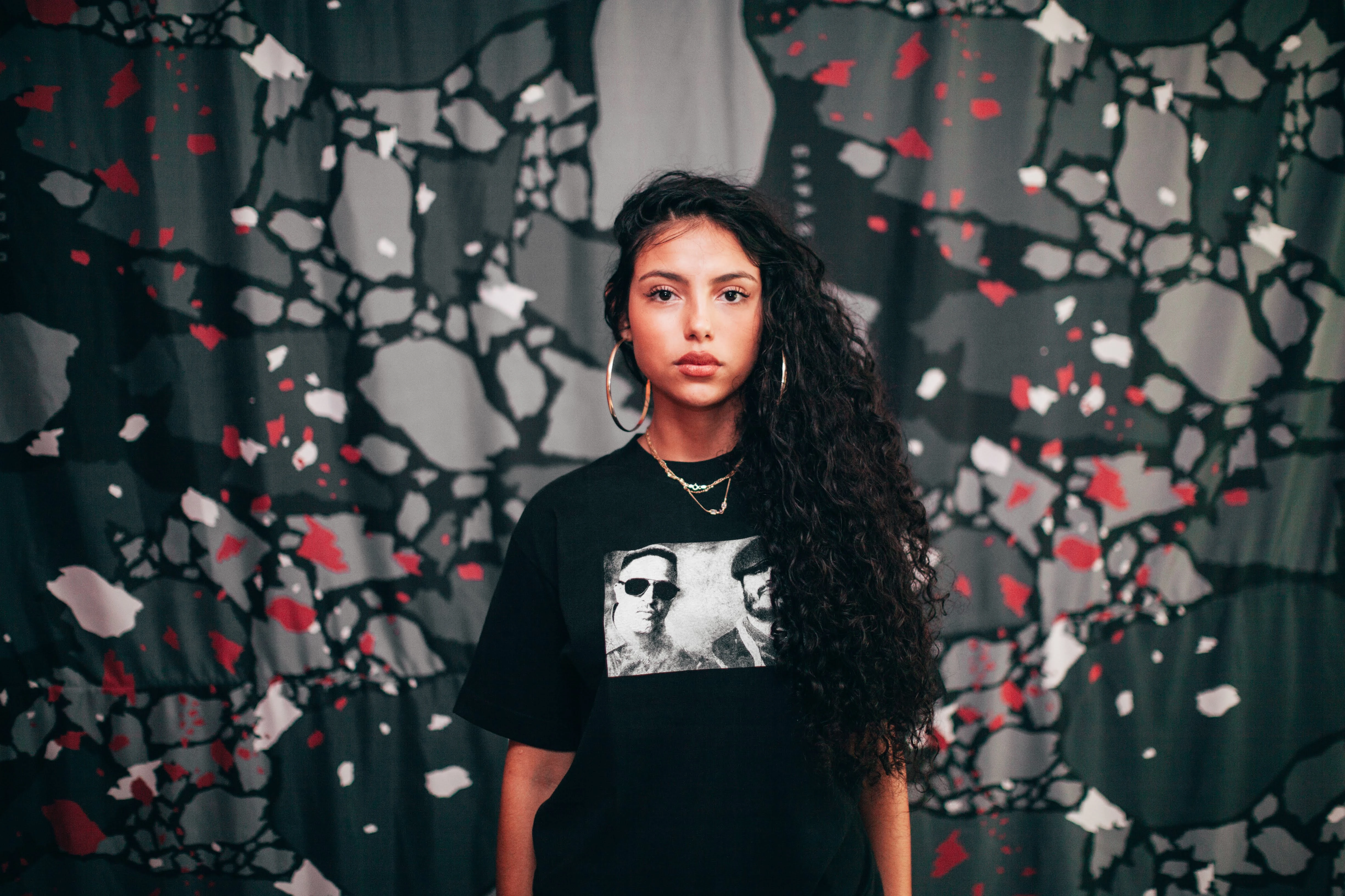 A model in a black graphic T-shirt from the collection against a patterned backdrop.