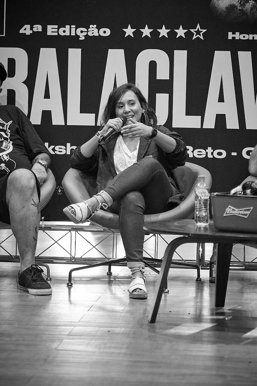 A speaker on stage at the fourth edition in front of the Semana Balaclava banner.