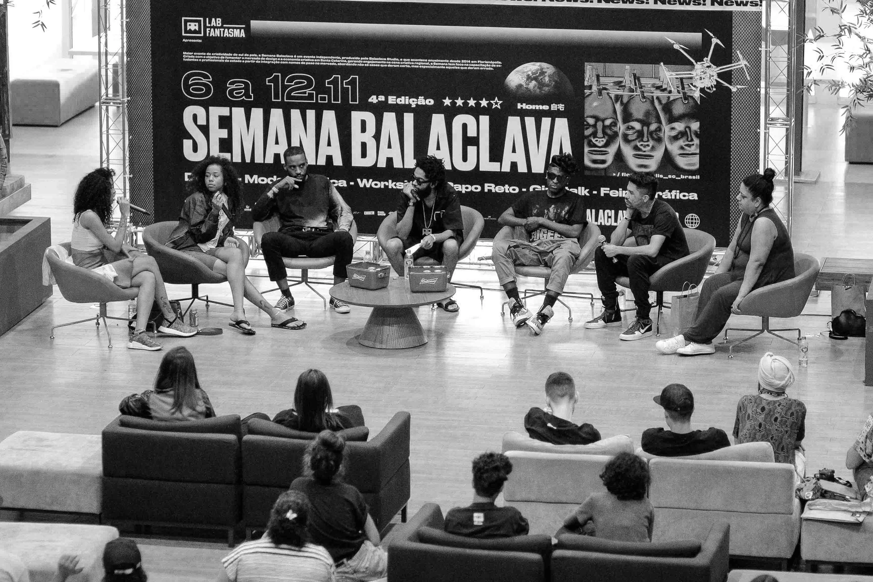 A panel of eight speakers on stage in an atrium with the audience seated in front.
