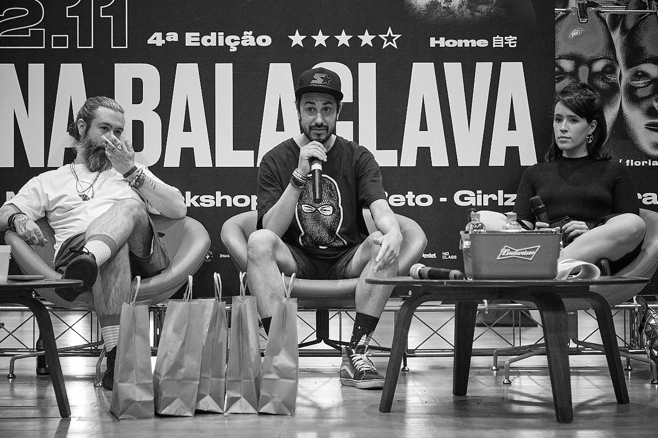 Three speakers on stage at the fourth edition in front of the Semana Balaclava backdrop.