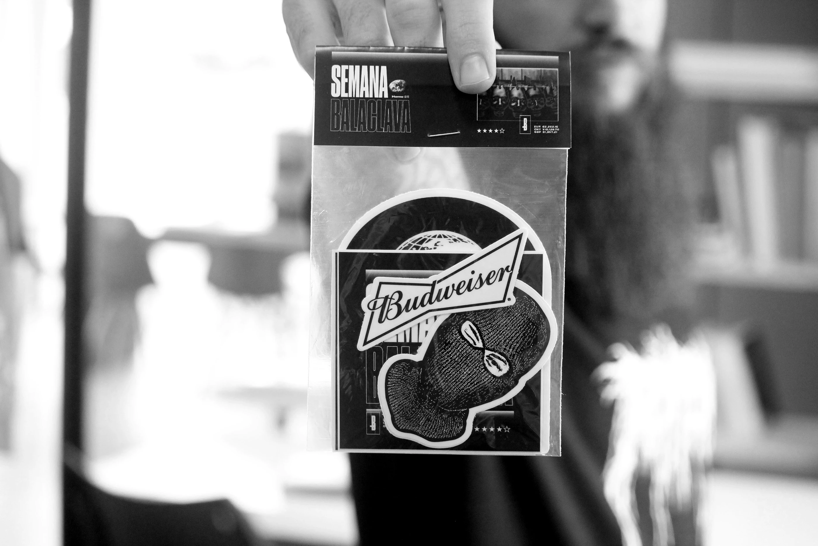 A hand holding a Budweiser-branded Semana Balaclava sticker pack.
