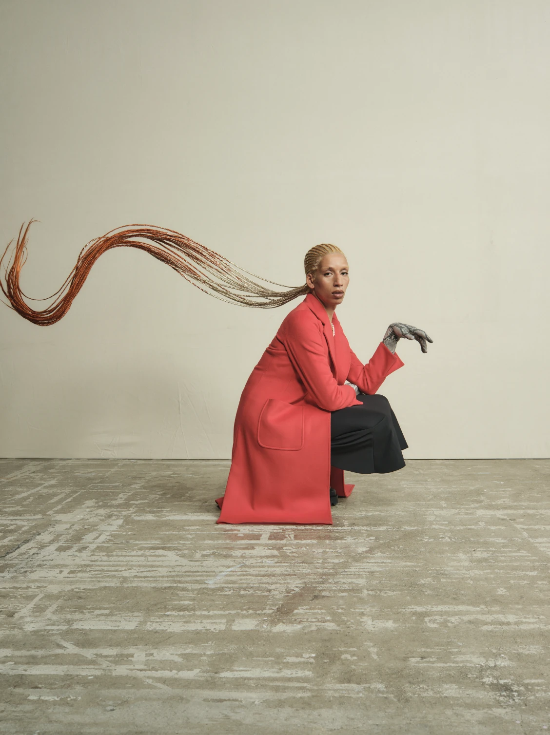 A model in a coral coat crouching, long braids streaming out behind.