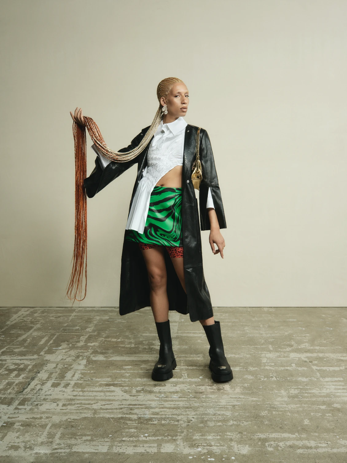 A model in a black leather coat, white shirt and green satin skirt holding out a long braid.
